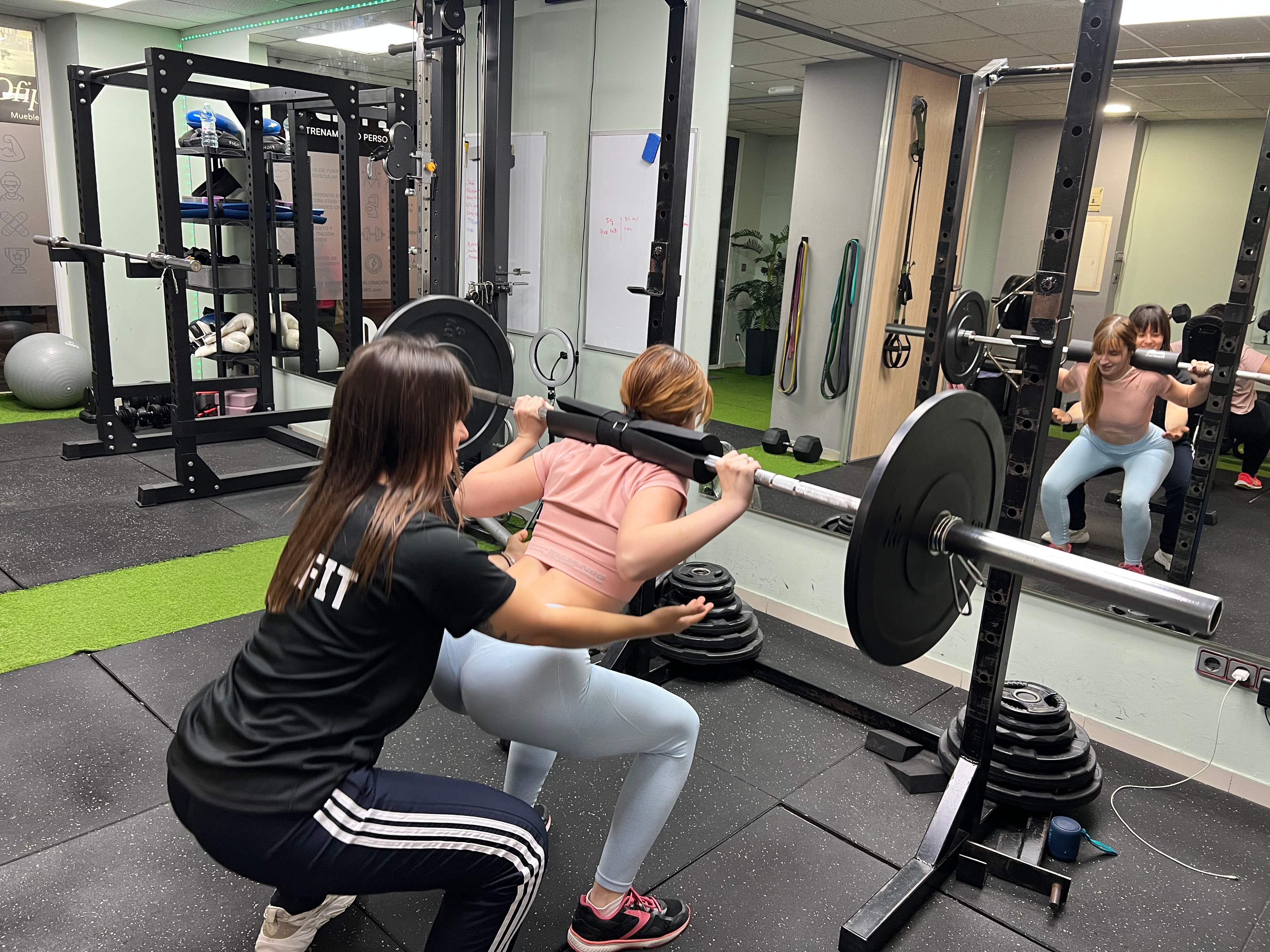 Entrenadora acompañando una sentadilla con barra